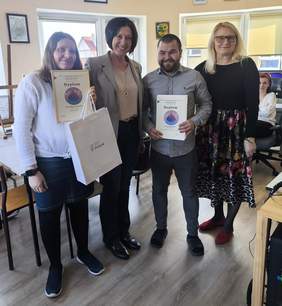 Pokaż zdjęcie: Do pamiątkowego zdjęcia pozują trzy kobieta oraz młody mężczyzna. Dwie osoby trzymają w ręku dyplomy.