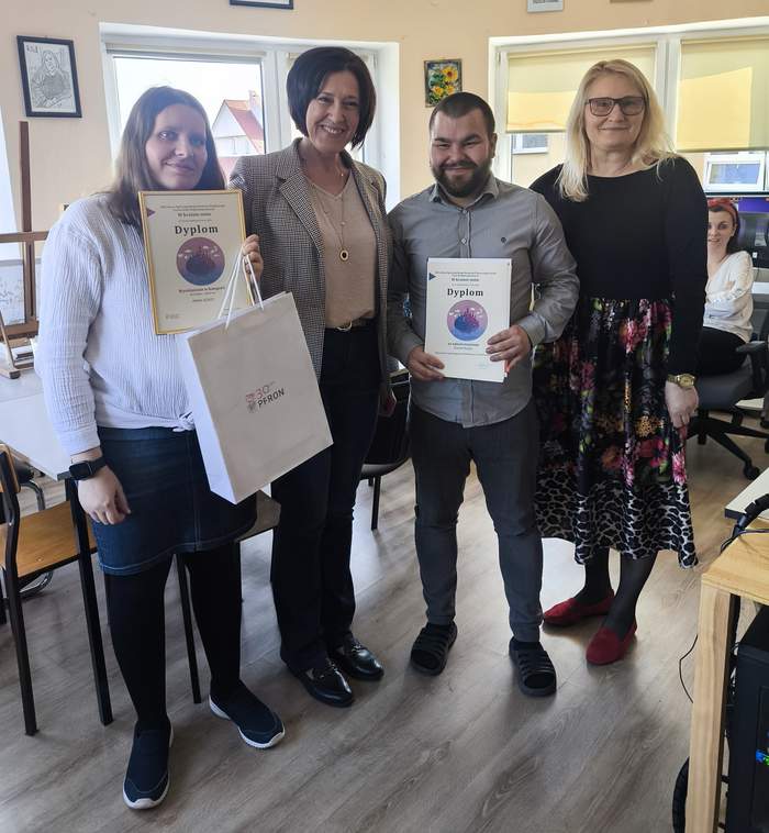 Pokaż zdjęcie: Do pamiątkowego zdjęcia pozują trzy kobieta oraz młody mężczyzna. Dwie osoby trzymają w ręku dyplomy.