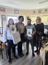 Do pamiątkowego zdjęcia pozują trzy kobieta oraz młody mężczyzna. Dwie osoby trzymają w ręku dyplomy.