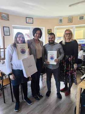 Do pamiątkowego zdjęcia pozują trzy kobieta oraz młody mężczyzna. Dwie osoby trzymają w ręku dyplomy.