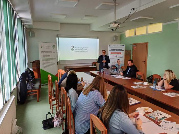 Pokaż zdjęcie: Specjalista ds. promocji i informacji na tle prezentacji, widoczni pracownicy PCPR, wszyscy są w sali konferencyjne