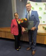 Monika Wac, dyrektor Oddziału Lubelskiego PFRON, i Mateusz Winiarski, dyrektor Oddziału Regionalnego KRUS w Lublinie, pozują do zdjęcia z kwiatami i pamiątkowym grawertonem podczas obchodów 35-lecia KRUS.