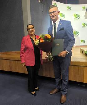 Monika Wac, dyrektor Oddziału Lubelskiego PFRON, i Mateusz Winiarski, dyrektor Oddziału Regionalnego KRUS w Lublinie, pozują do zdjęcia z kwiatami i pamiątkowym grawertonem podczas obchodów 35-lecia KRUS.