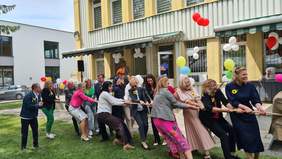 Pokaż zdjęcie: Na zewnątrz kilkanaście osób przeciąga linę. 