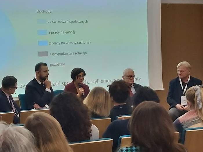 Wystąpienie prelegentów konferencji. Za stołem sieci pięć osób, w tle ekran na którym wyświetlana jest prezentacja.