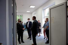 przez otwarte drzwi widać 6 osób w maseczkach w nowym pomieszczeniu, pomieszczenie jest jasne z uwagi na okna 