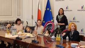 Pokaż zdjęcie: Trzy matki z dziećmi siedzą przy stole, obok nich stoi kobieta, która jest tłumaczem.