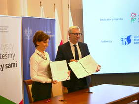 Pokaż zdjęcie: Dwie osoby trzymają podpisana umowę.