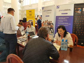 ludzie rozmawiają przy stołach na tle banerów