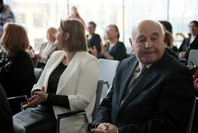 Pokaż zdjęcie: Zdjęcie sali konferencyjnej i zaproszonych gości, na pierwszym tle kobieta w białej marynarce oraz mężczyzna w garniturze