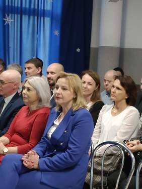 Pokaż zdjęcie: Zdjęcie publiczności siedzącej na krzesłach, zbliżenie na ładną blondynkę w niebieskim garniturze, obok niej jedno miejsce jest wolne