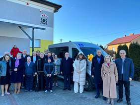 Zdjęcie grupowe kilkunastu osób na tle nowego busa, z lewej strony widok fragmentu budynku