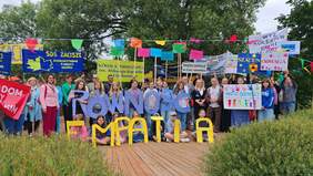 Pokaż zdjęcie: Grupa ludzi – dzieci, młodzież i dorośli – bierze udział w Marszu Godności Osób z Niepełnosprawnościami. Trzymają kolorowe transparenty i plakaty z hasłami: „RÓWNOŚĆ”, „EMPATIA”, „SZACUNEK”, „ODWAGA”, „GODNOŚĆ”, „INTEGRACJA” oraz nazwami szkół i instytucji wspierających.