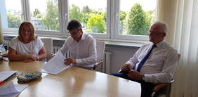 Pokaż zdjęcie: przy stole 3 osoby przy podpisaniu umowy, od lewej kobieta obok dwóch mężczyzn