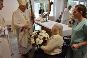 Pokaż zdjęcie: Ksiądz biskup święcący budynek i kaplice otrzymuje wiązankę kwiatów od jednej z podopiecznych