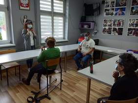 Pokaż zdjęcie: Na zdjęciu psycholog i uczestnicy WTZ podczas treningu zakładania maseczek, przyłbic i mycia rąk 