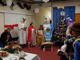 Pokaż zdjęcie: Inscenizacja jasełek podczas spotkania wigilijnego w Warsztatach Terapii Zajęciowej w Ogrodniczkach, przedstawiająca uczestników w barwnych strojach, przy świątecznie udekorowanej choince.