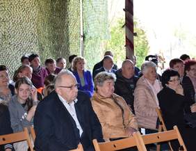 Pokaż zdjęcie: Pod namiotem na krzesełkach siedzą zaproszeni goście, spoglądają w kierunku sceny