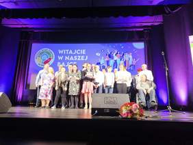 Pokaż zdjęcie: Na scenie duża grupa osób śpiewa wesołą piosenkę.