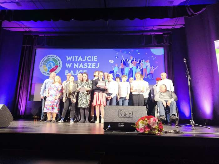 Pokaż zdjęcie: Na scenie duża grupa osób śpiewa wesołą piosenkę.