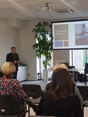 Sala konferencyjna. Na krzesłach siedzą przedstawiciele podmiotów publicznych. Przed uczestnikami stoi pan Łukasz Żmuda - Dyrektor Oddziału Opolskiego PFRON. Na ekranie na ścianie wyświetlana jest prezentacja dot. składania skarg na brak dostępn