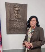 Elegancko ubrana kobieta pozuje do zdjęcia na tle tablicy pamiątkowej