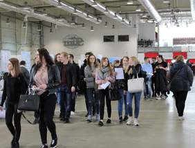 Pokaż zdjęcie: Grupa młodych ludzi spaceruje wśród stoisk wystawowych