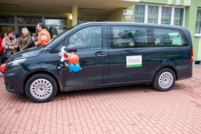 Pokaż zdjęcie: Przed budynkiem stoi samochód marki bus w środku sziedzą dzieci. Auto jest ozdobione balonami.