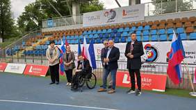 Pokaż zdjęcie: Uczestnicy i goście stoją na stadionie w Lublinie podczas zawodów łuczniczych „Koziołek 2026”; w tle trybuny, flagi i banery promujące wydarzenie.