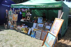 Pokaż zdjęcie: Stoisko promocyjne warsztatów terapii zajęciowej, zawiera prace takie jak obrazy, rzeźby, ceramikę, makatki, ozdoby, zabawki