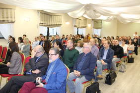 Pokaż zdjęcie: Zdjęcie sali konferencyjnej, na czerwonych krzesełkach siedzą uczestnicy konferencji