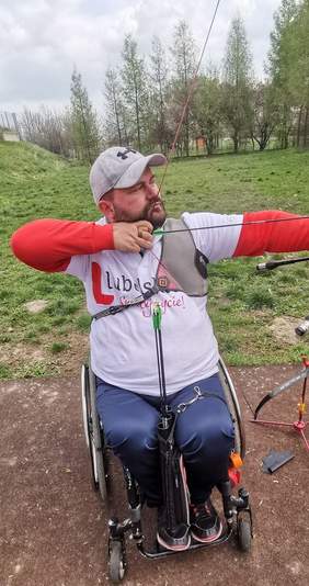 Pokaż zdjęcie: Mężczyzna na wózku inwalidzkim celujący z łuku do tarczyu 