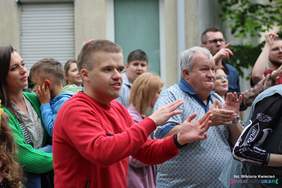 Pokaż zdjęcie: Zdjęcie publiczności stojącej przed sceną, na pierwszym planie zbliżenie na chłopca w czerwonej bluzie machającego rękami.