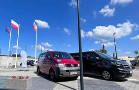 Pokaż zdjęcie: Mikrobus dofinansowany ze środków PFRON, zakupiony na rzecz WTZ w Harbutowicach. Dwa mikrobusy stoją na parkingu na tle błękitnego nieba.