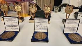 Pokaż zdjęcie: Na stole stoją trzy medale honorowe w niebieskim pudełku, za nimi statuetki z napisem 30 lat PSONI.