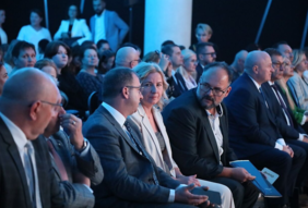 Pokaż zdjęcie: Zdjęcie zaproszonych gości siedzących na widowni, zbliżenie na kobietę blondynkę w jasnym garniturze.