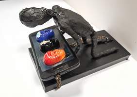 Pokaż zdjęcie: Zdjęcie rzeźby w kolorze czarnym przedstawiająca człowieka klęczącego nad telefonem i przykutego do niego łańcuchami. Na telefonie są trzy twarze z logo facebook, instagram i twitter