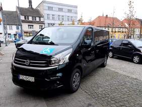 Pokaż zdjęcie: Nowy bus dla ŚDS w Drezdenku w kolorze czarnym stoi na parkingu, a w tle rynek w Drezdenku
