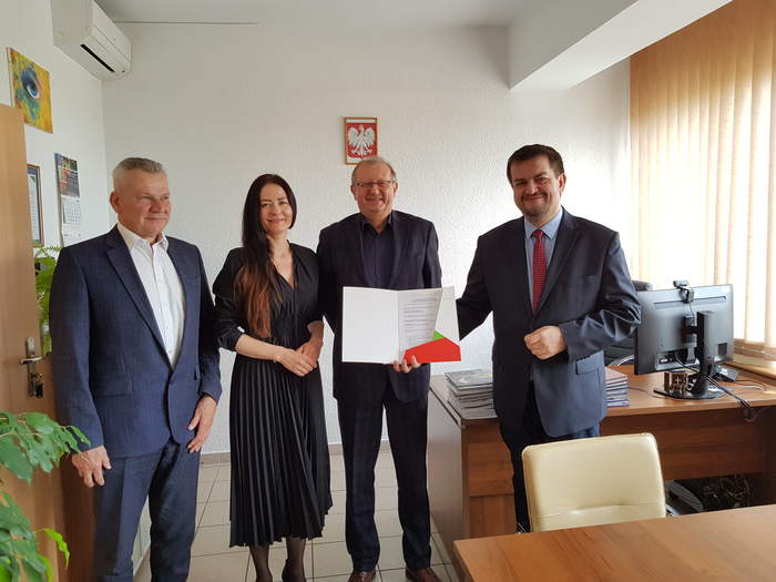 Pokaż zdjęcie: W gabinecie Dyrektora Oddziału PFRON w Zielonej Górze stoją obok siebie władze Powiatu Zielonogórskiego oraz Dyrektor Oddziału PFRON w Zielonej Górze, wszyscy są uśmiechnięci, Dyrektor trzyma w ręku teczkę z umową