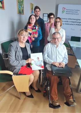 Pokaż zdjęcie: Kobiety i mężczyźni, w tym mężczyzna na wóżku inwalidzkim w sali konferencyjnej pozuja do zdjęcia.