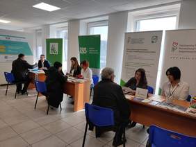 Pokaż zdjęcie: Sala Obsługi Klientów. przy oknie stoją trzy podwójne stoliki przy których stoiska informacyjne mają pracownicy PFRON,KRUS i ZUS. Za stolikami stoją banery reklamowe poszczególnych instytucji.