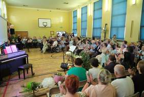 Pokaż zdjęcie: Zdjęcie obejmujące salę gimnastyczną na której odbywał się jubileusz, pokazano zaproszonych gości oraz mieszkańców domu.