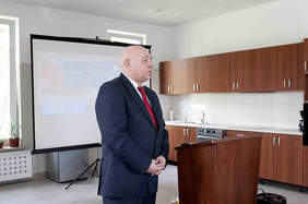 Pokaż zdjęcie: Przy mównicy stoi starszy mężczyzna w ciemnym garniturze