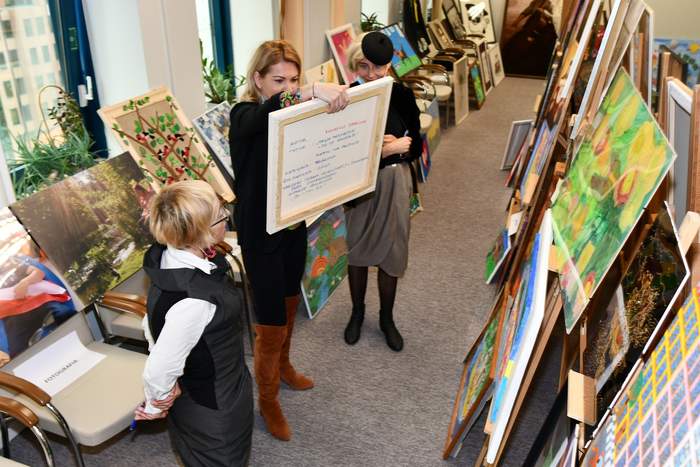 Plan zdjęcia stanowi sala w której na sztalugach ustawione są prace plastyczne. W centrum fotografii stoją członkowie komisji konkursowej, Pani Bogna Jarzemska-Misztalska, trzyma w rękach jedną z prac.