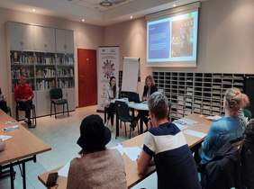 Pokaż zdjęcie: sala konferencyjna dookoła siedzą osoby przy stolikach  na środku rzutnik  prezenuje projekt Powrót do zdrowia powrót do pracy , po środku pracownik Oddziału przedstawia możliwości wsparcia dla osób z Ukrainy