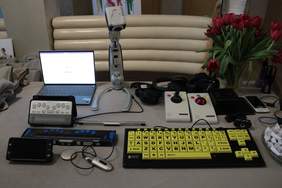 Pokaż zdjęcie: Stół na którym stoją urządzenia wspomagające komunikację, klawiatura, laptop, cyber oko