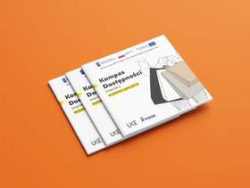 Zdjęcie jest infografiką. Na pomarańczowym tle znajdują się trzy egzemplarze poradnika "Kompas dostępności". Widać jedynie okładki. 