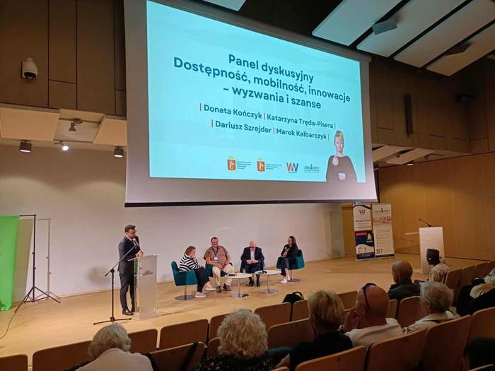 scena, na której siedzi kilka osób, na ekranie wyświetla się napis panel dyskusyjny