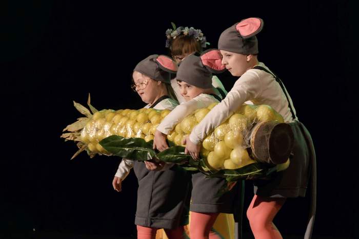 Pokaż zdjęcie: Na scenie stoją dwaj chłopcy i dziewczynka przebrani za myszki. Wspólnie trzymają ogromną kukurydzę