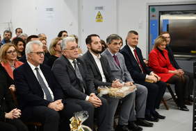 Pokaż zdjęcie: Zdjęcie pierwszego rzędu zaproszonych gości, na krzesłach siedzą mężczyźni w średnim wieku, ubrani w ciemne garnitury